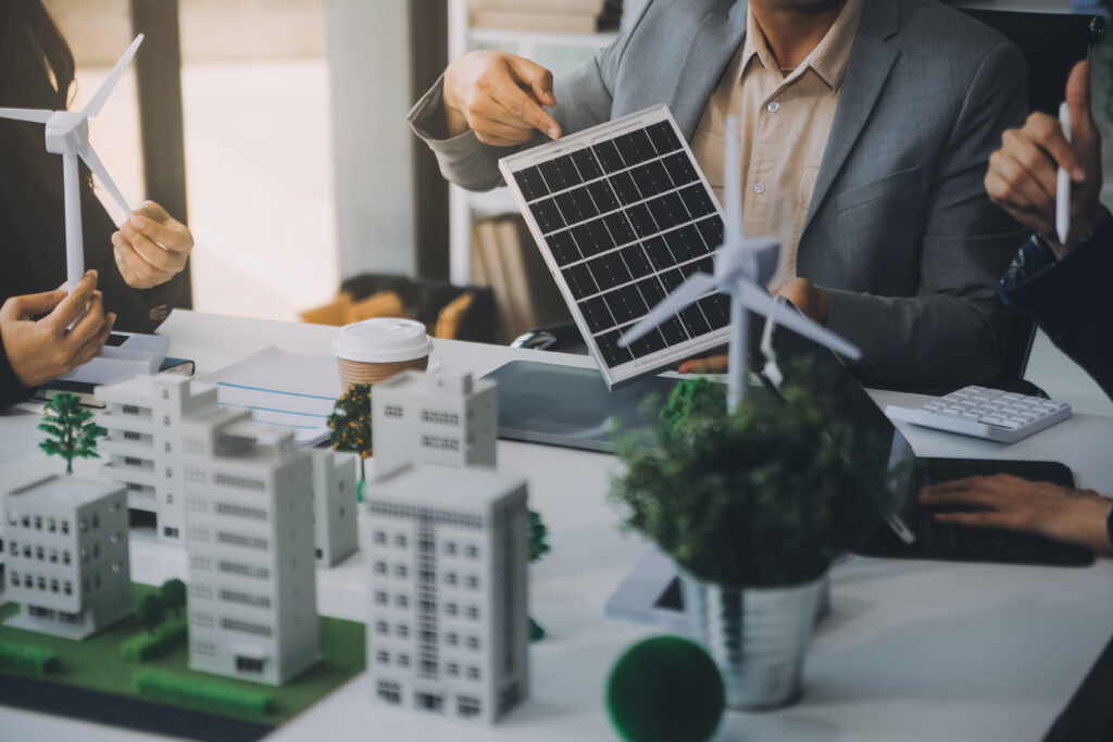 Business meeting on solar energy solutions with models of buildings, wind turbines, and solar panels.