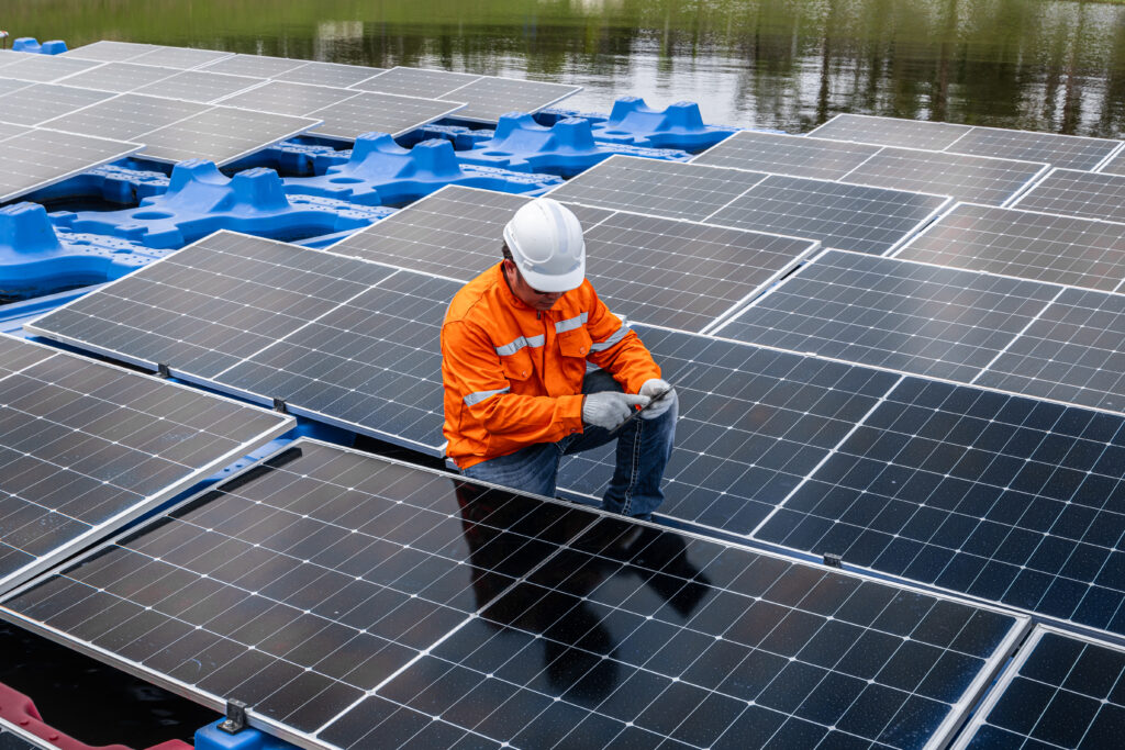 Worker in orange vest inspecting floating solar panels on water