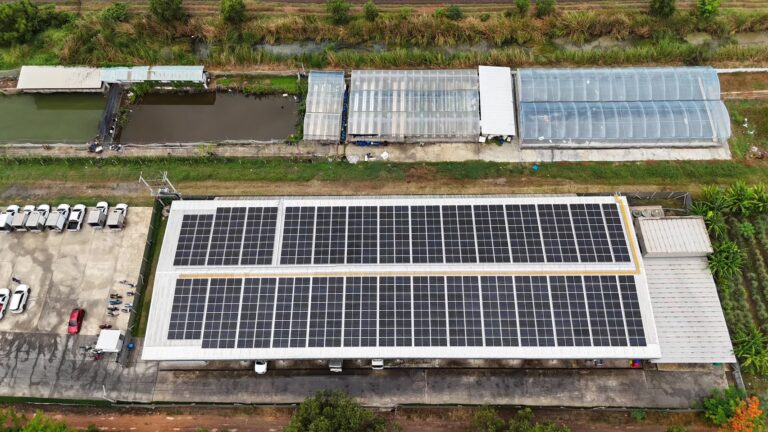 Aerial view of a solar panel installation on a large building, with greenhouses and ponds nearby.