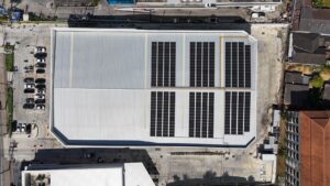 Aerial view of a large warehouse roof with solar panels installed, featuring a parking lot.