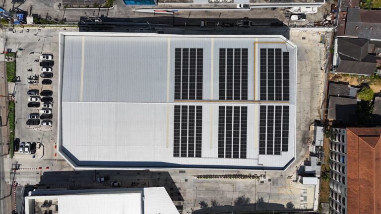 Aerial view of a large warehouse roof with solar panels installed, featuring a parking lot.