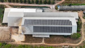 Aerial view of a factory with a large solar panel installation on the roof.