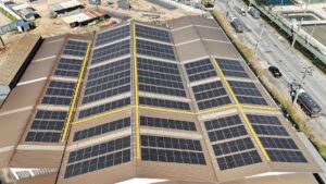 Aerial view of a large warehouse roof covered in solar panels, with trucks nearby.