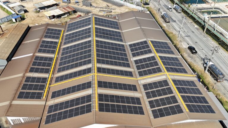 Aerial view of a large warehouse roof covered in solar panels, with trucks nearby.