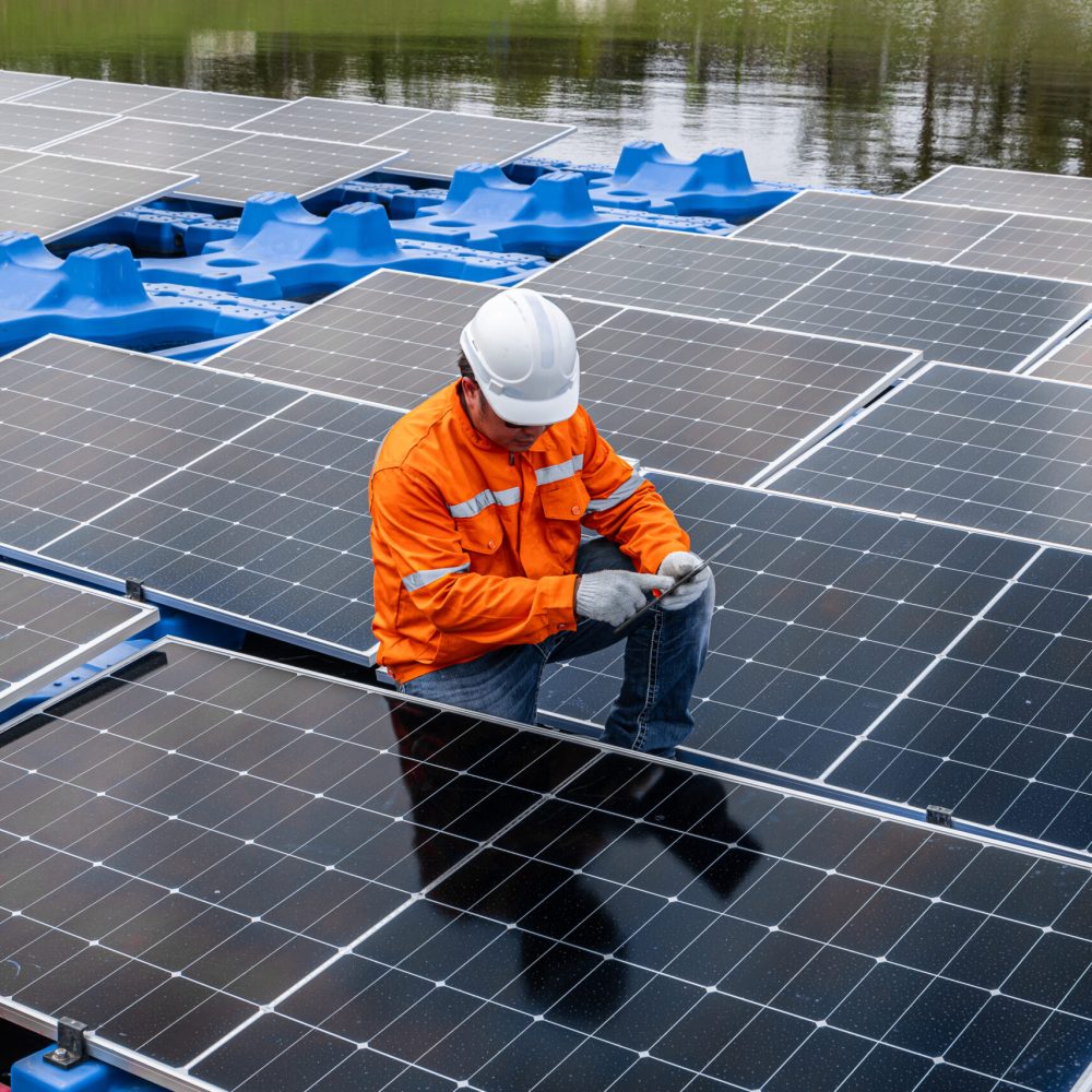 Worker in orange vest inspecting floating solar panels on water